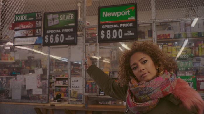 Person inside store pointing toward cigarette price signs displayed behind counter.